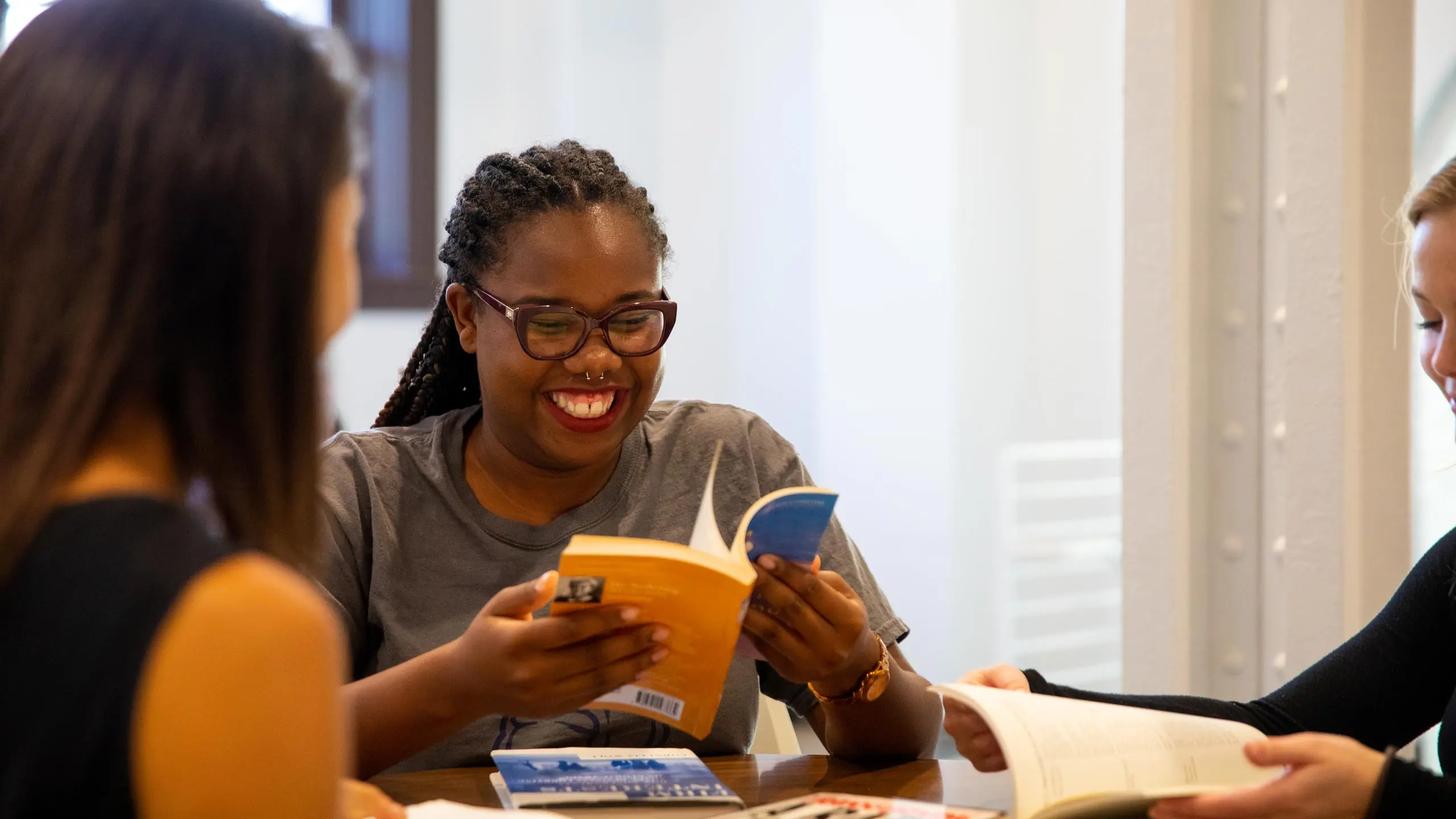 Three female students sitting around a able reading books while smiling