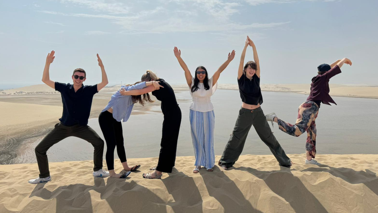 A group of six students spelling "HOYAS" with their bodies in the desert in Qatar.