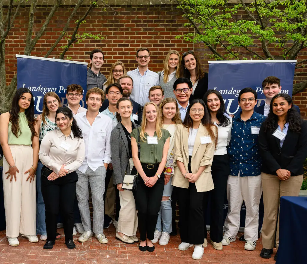 Nguyen stands with a large group of classmates in front of banners for the Landegger Program in International Business Diplomacy.