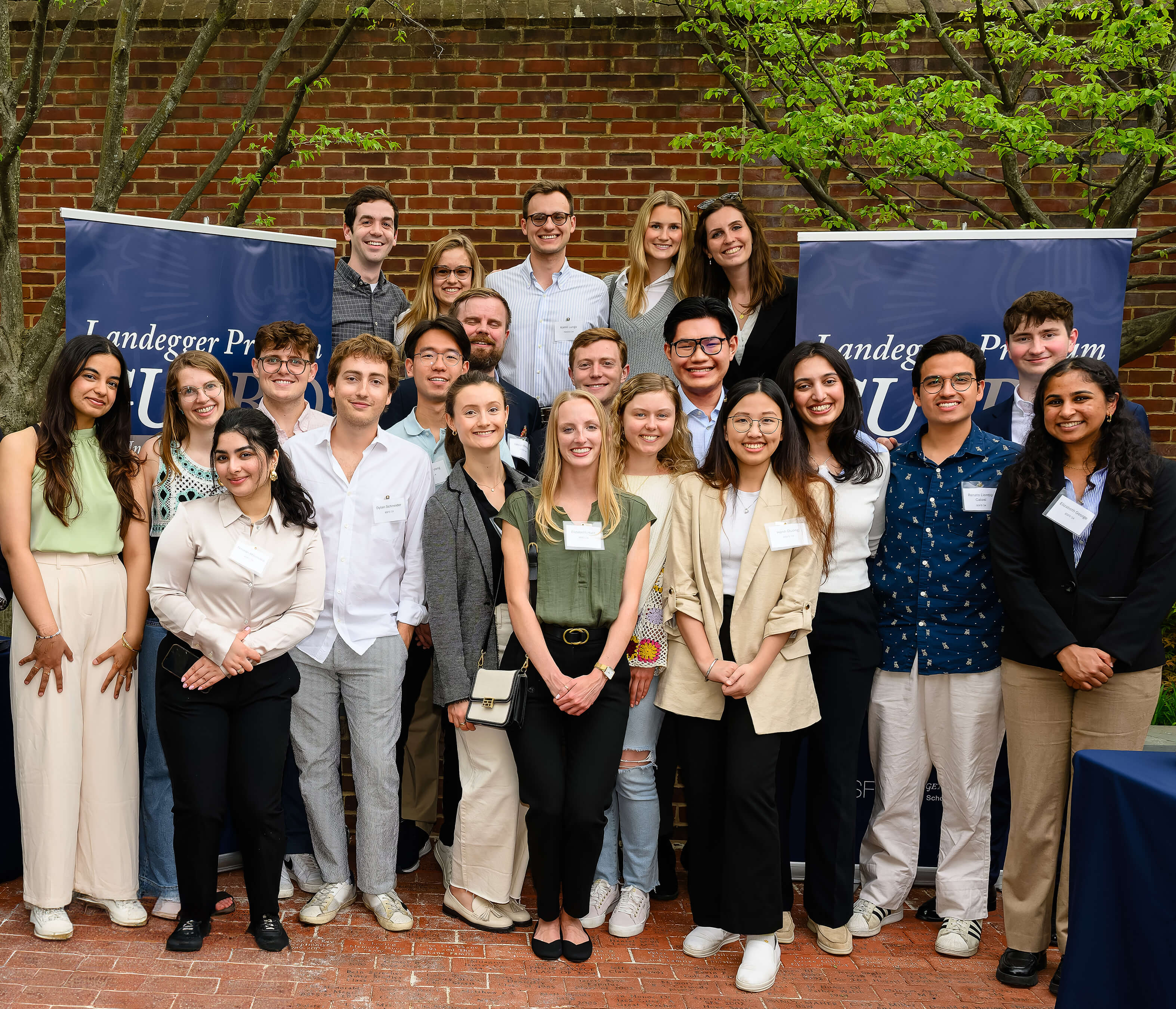 Nguyen stands with a large group of classmates in front of banners for the Landegger Program in International Business Diplomacy.