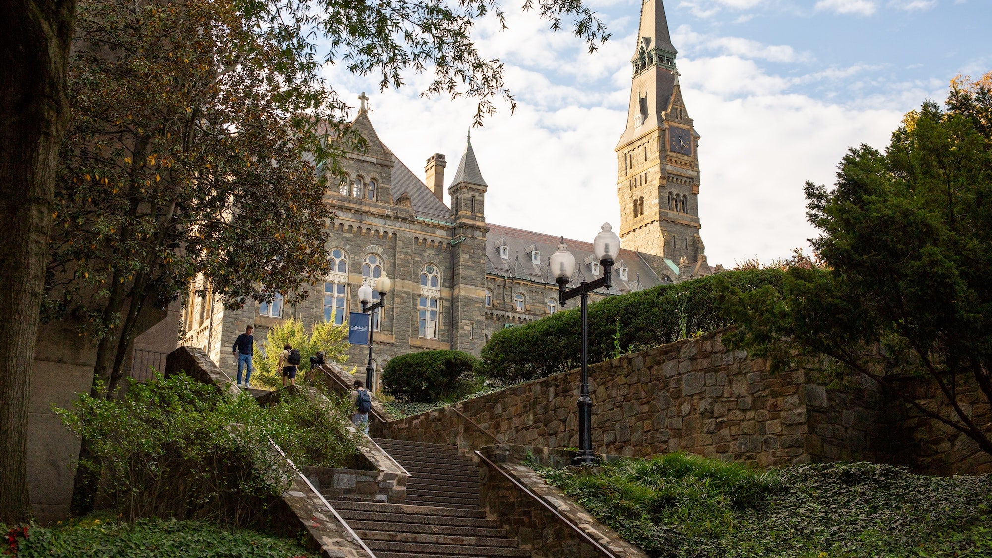 Students walking on stairs to Lauinger Library on Georgetown University's campus with Healy Hall in the background during a sunny summer day