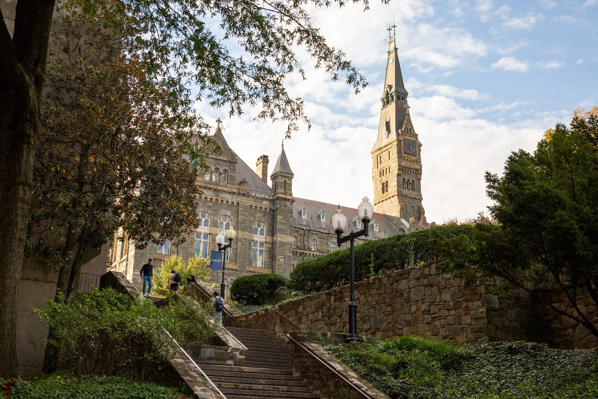 Students walking on stairs to Lauinger Library on Georgetown University's campus with Healy Hall in the background during a sunny summer day