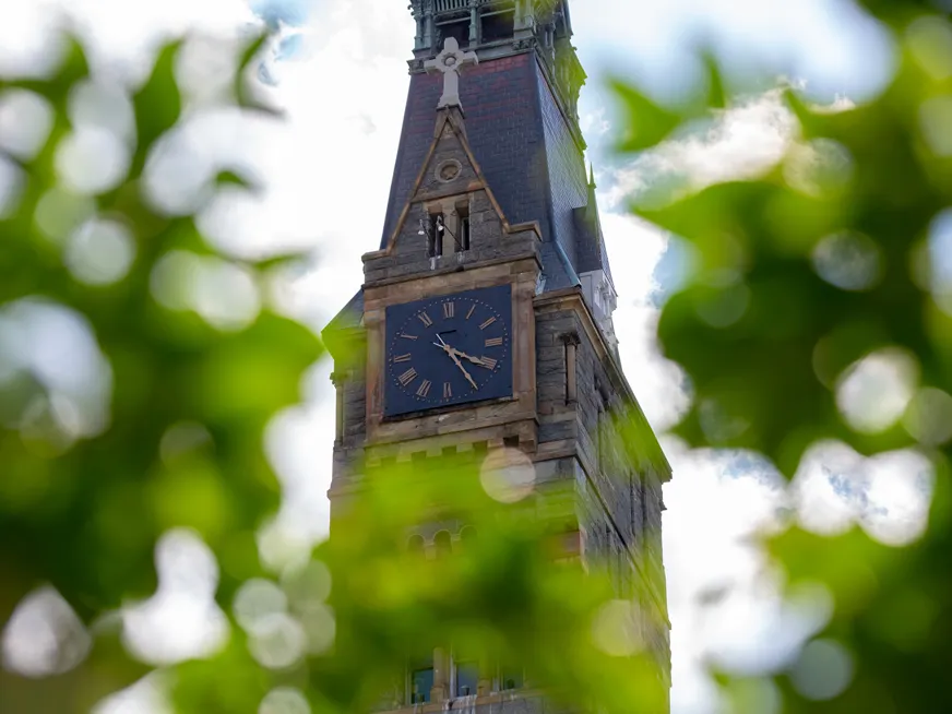 Healy hall tower clock in focus, with green tree leaves out of focus.