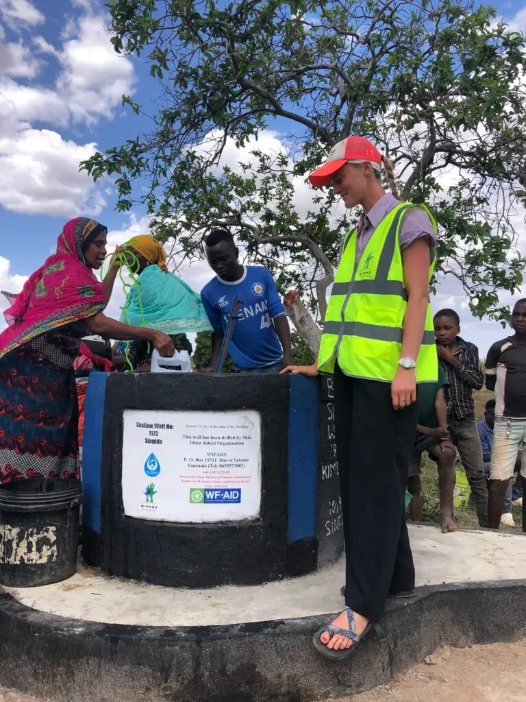 Marina McPhail wearing a yellow reflective vest stands next to a well in rural Singida, Tanzania.