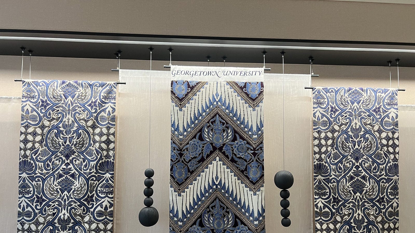 Three Indonesian batiks hanging in a display, all in shades of blue and grey.