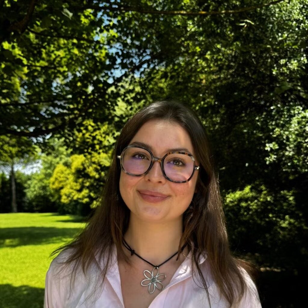 Jessica Pretorius wearing a pink button-down shirt with a flower shaped necklace and glasses.