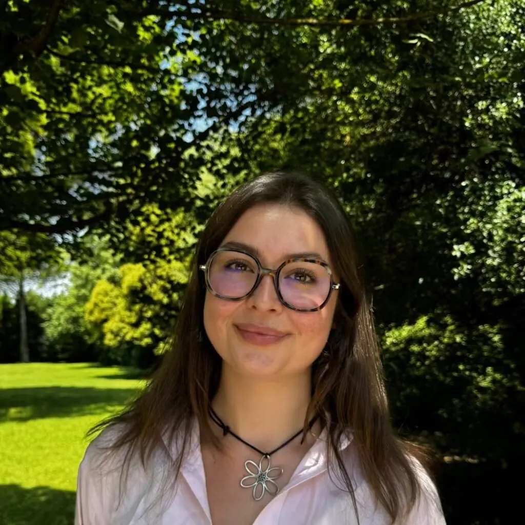 Jessica Pretorius wearing a pink button-down shirt with a flower shaped necklace and glasses.