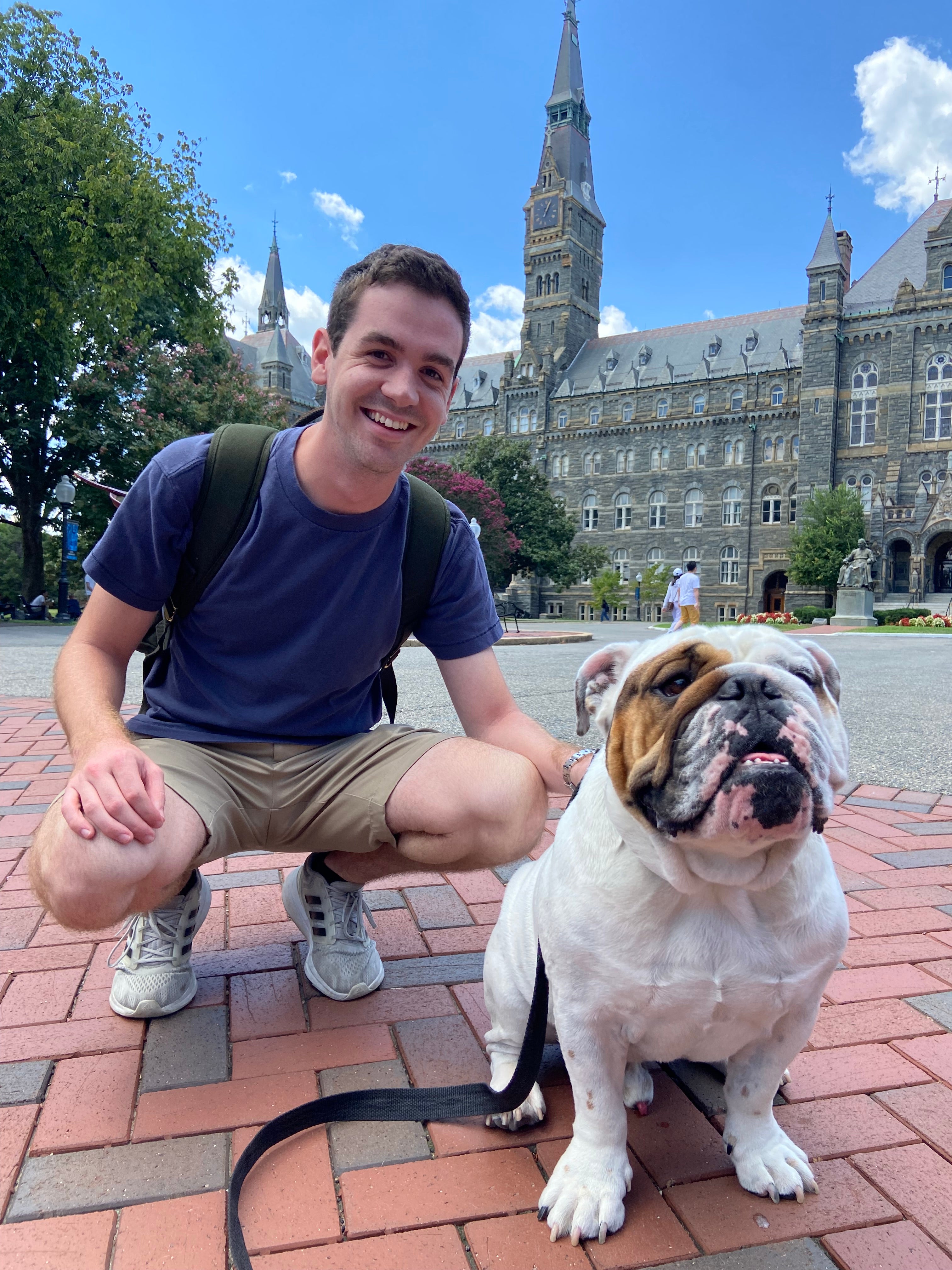 Joe Locher crouches next to Jack the Bulldog with Healy Hall behind him.