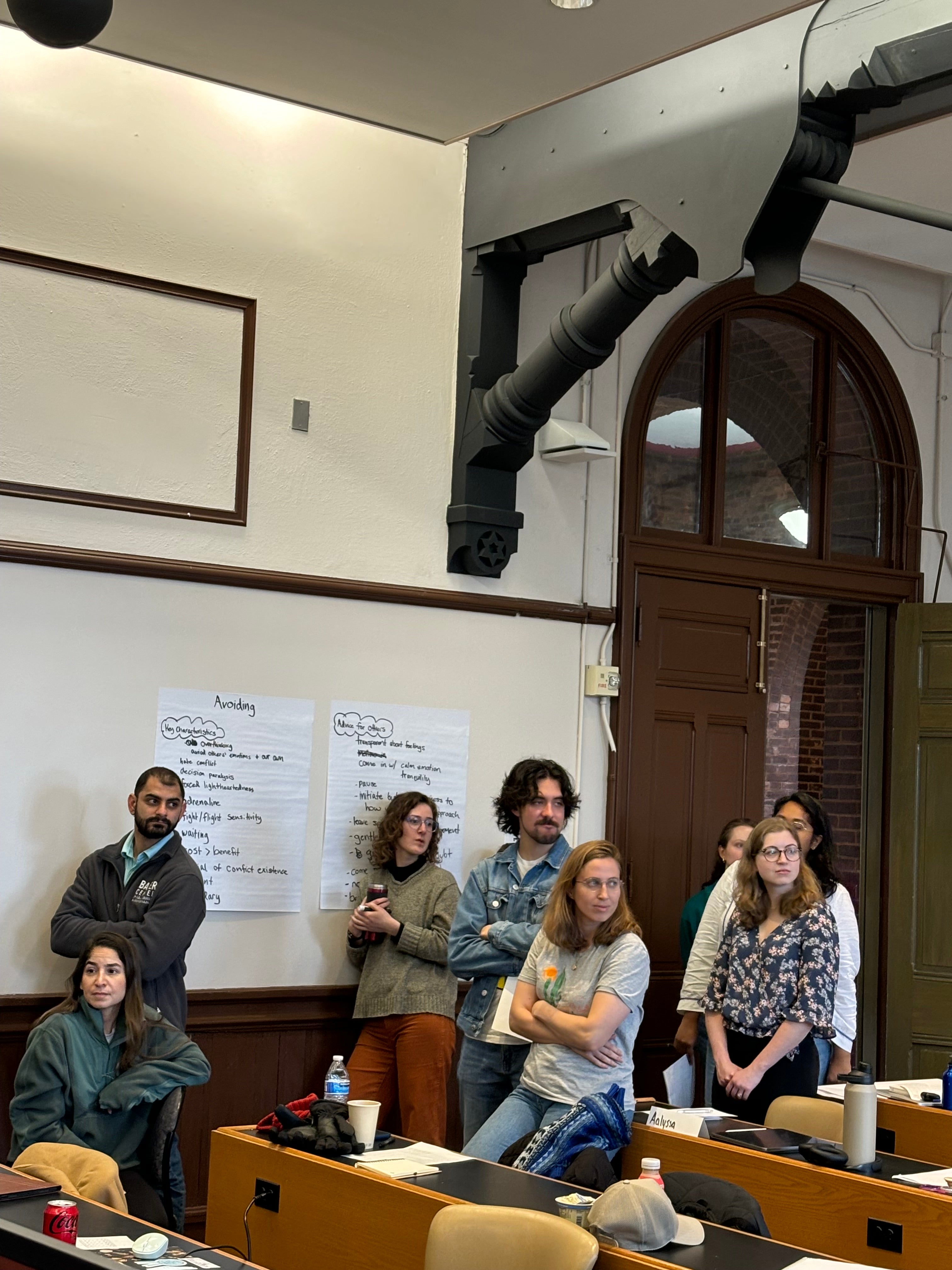 Korban stands in a classroom with some classmates standing and some sitting.