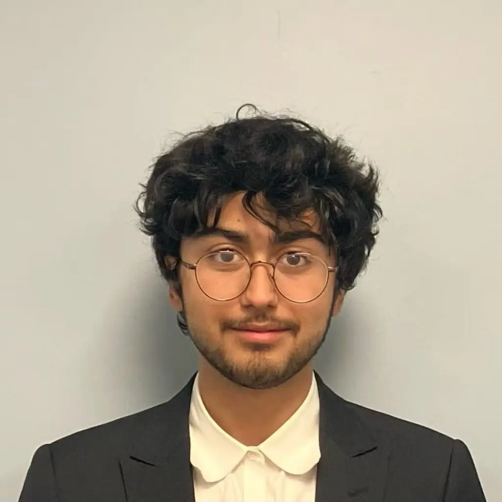 Jon Plummer wearing a black blazer and cream shirt with glasses.