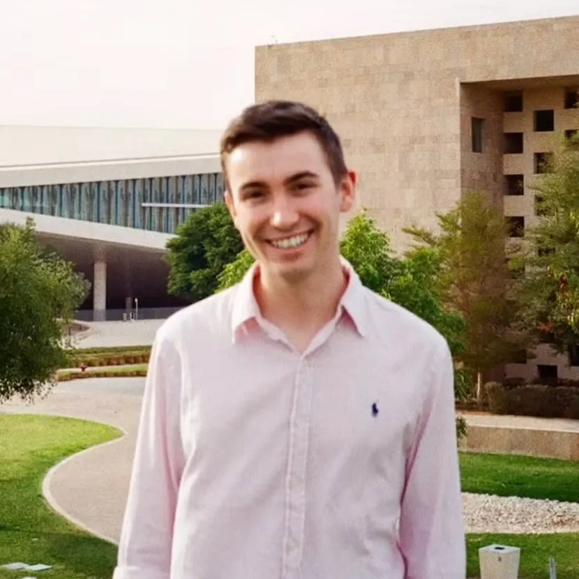 Josh Ford outside of the Education City in Qatar. Behind him buildings surrounded by green trees.