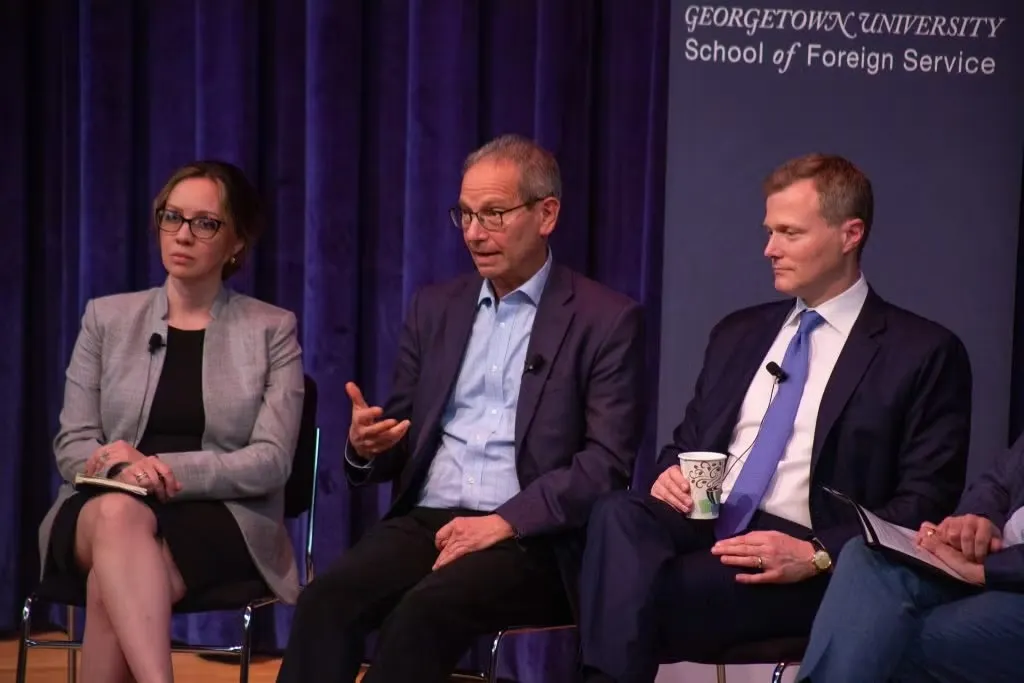Three panelists seated on stage at Georgetown University, engaged in discussion during a panel event.