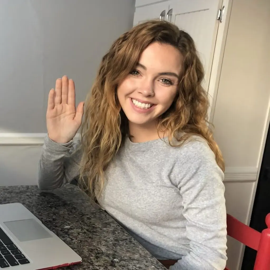Kendall Trelegan waving at the camera from a desk, wearing a gray shirt.