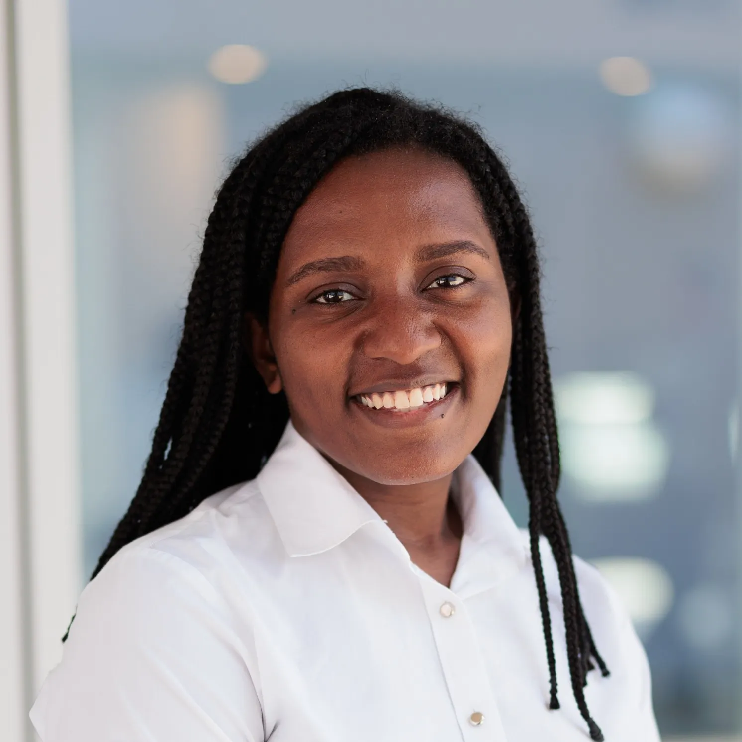 Portrait of a smiling individual with braided hair, wearing a white shirt.
