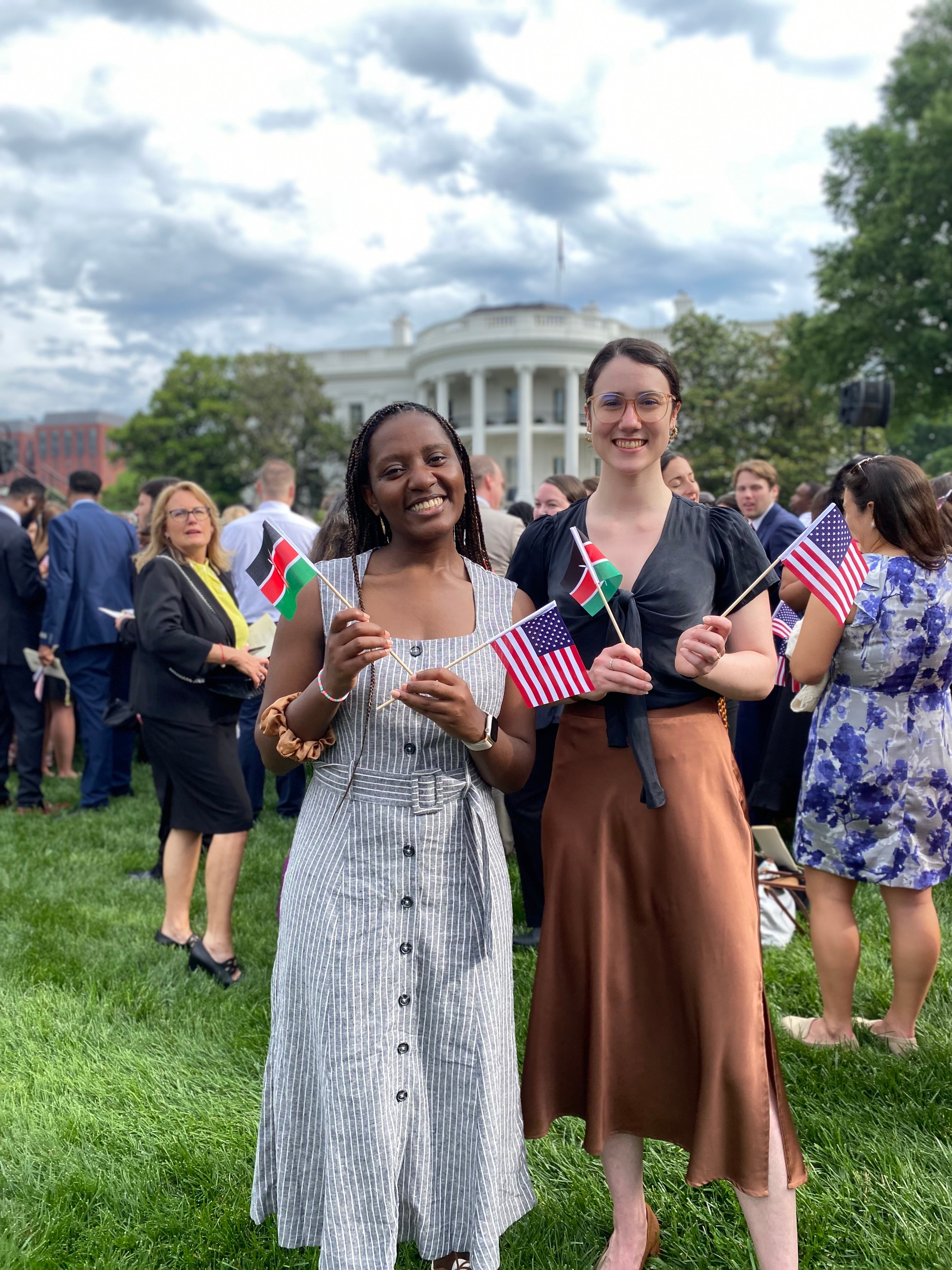 Two individuals holding flags, including the American flag, smiling at an event on the White House lawn.