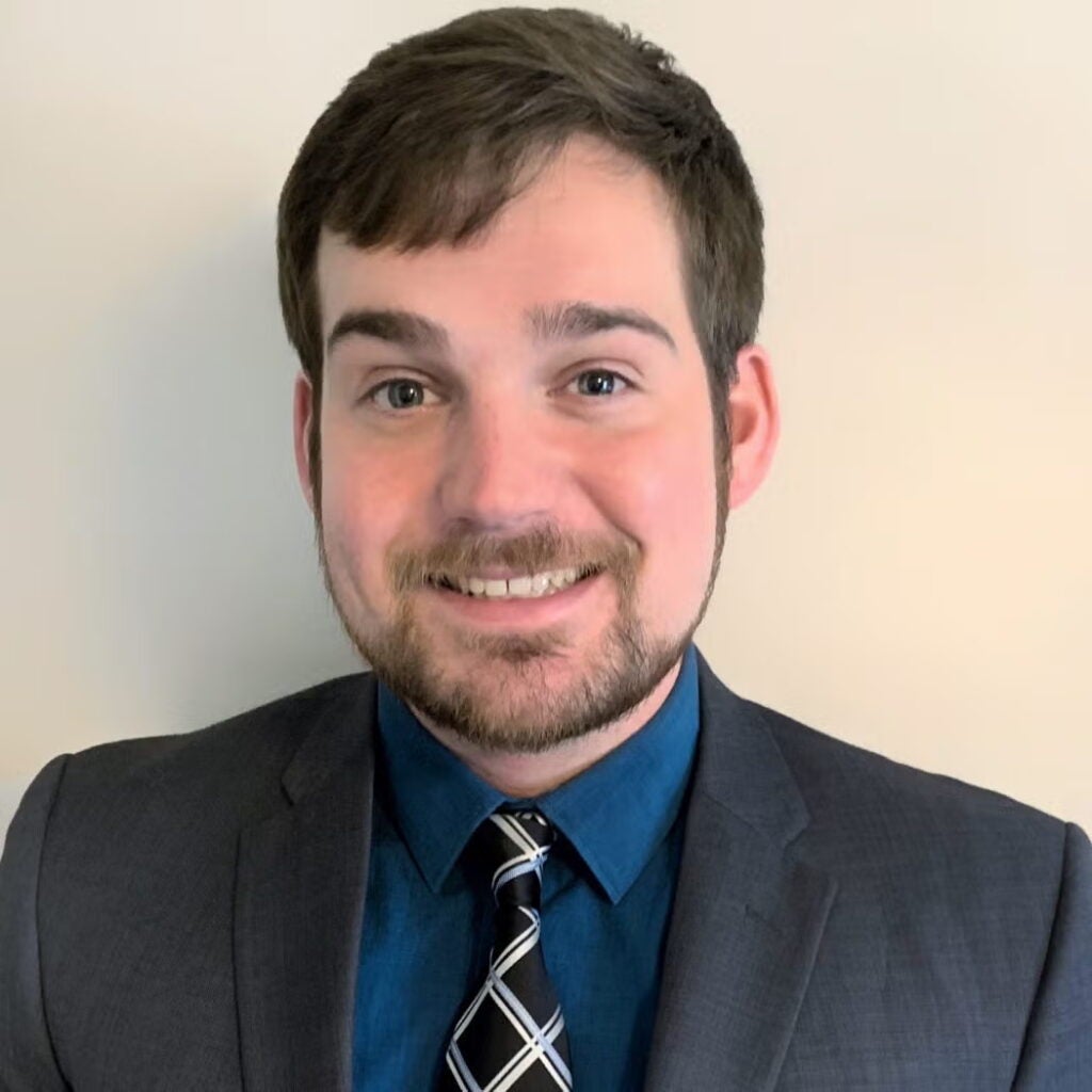 Kyle Clements wearing a dark blazer and tie.