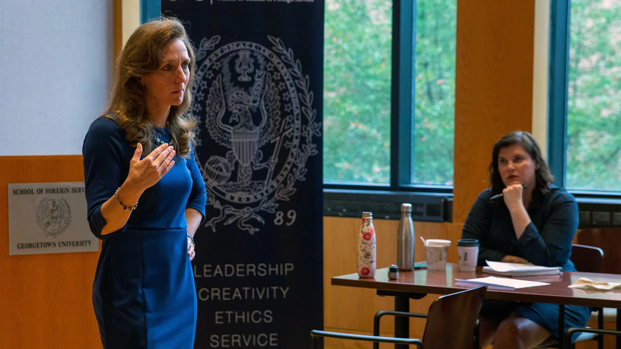 Laura Lane speaking with students at a campus venue. Behind her, a banner with the Georgetown crest and the words leadership, creativity, ethics, service.