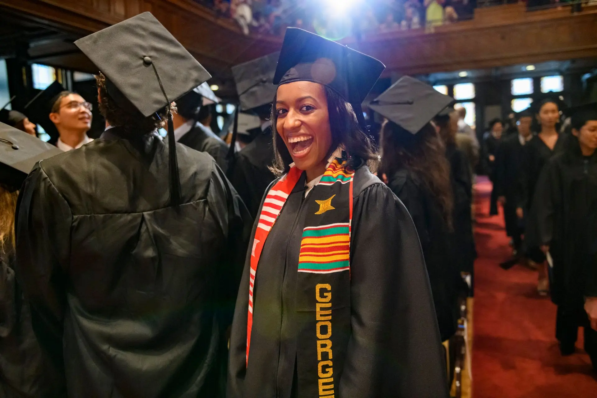 MSFS Graduate student wearing commencement regalia and smiling broadly.