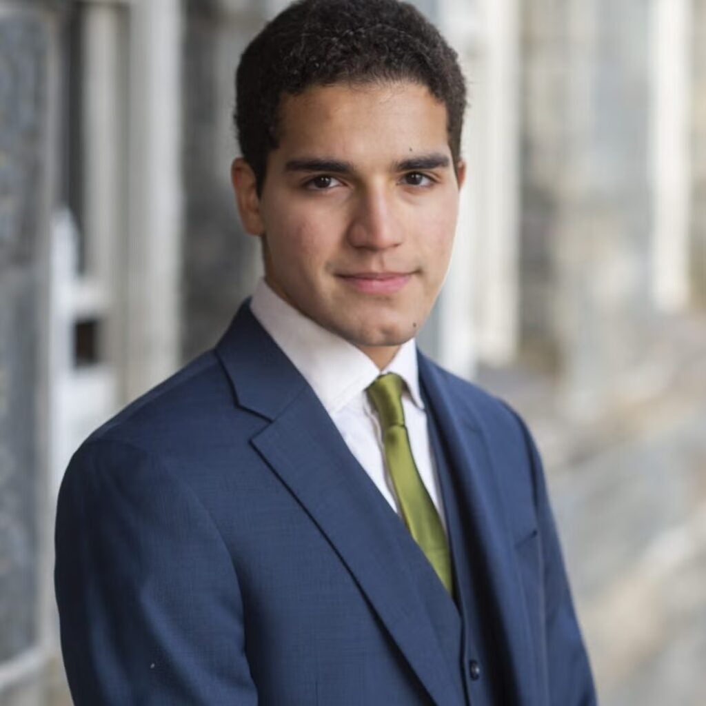 Marco Perez wearing a navy blue suit, a white button-down shirt with a green tie.