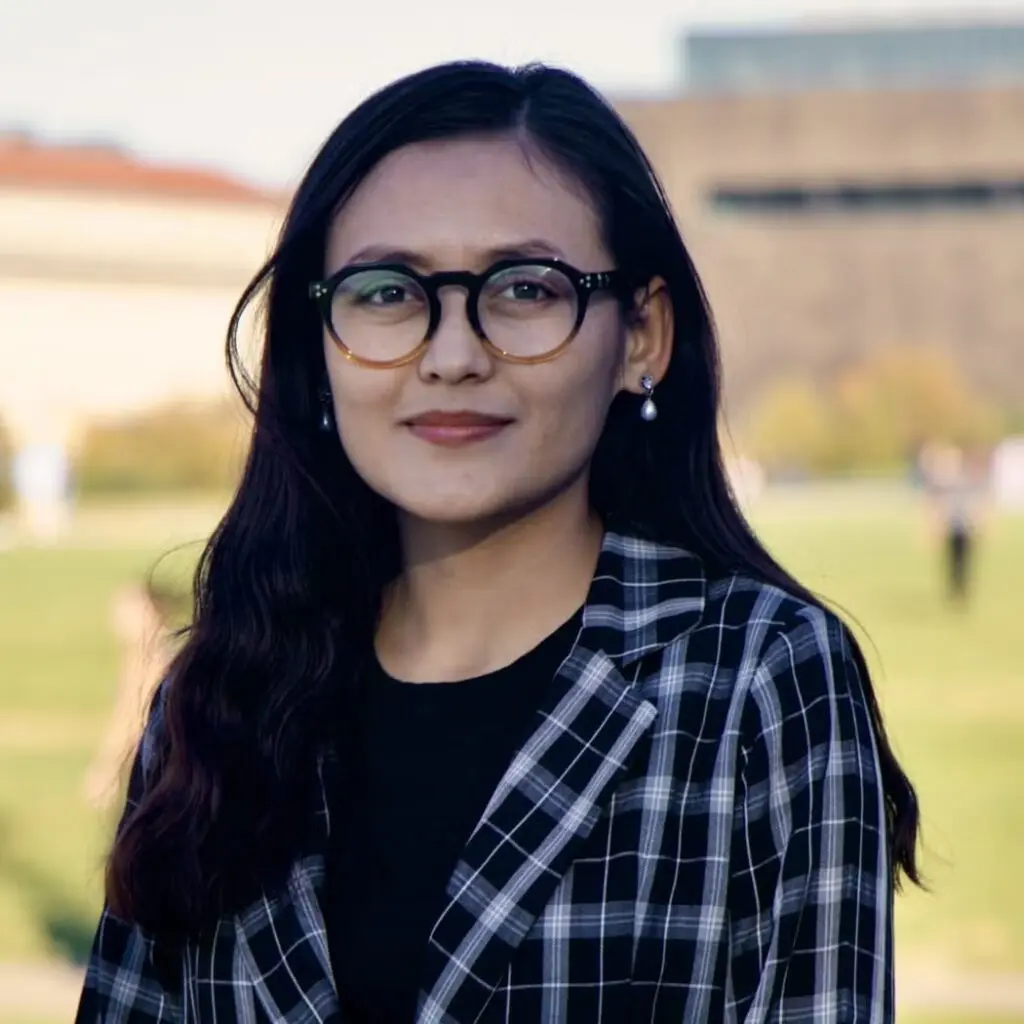 Marzia Amiri wearing a white shirt and a black and white plaid blazer with glasses.