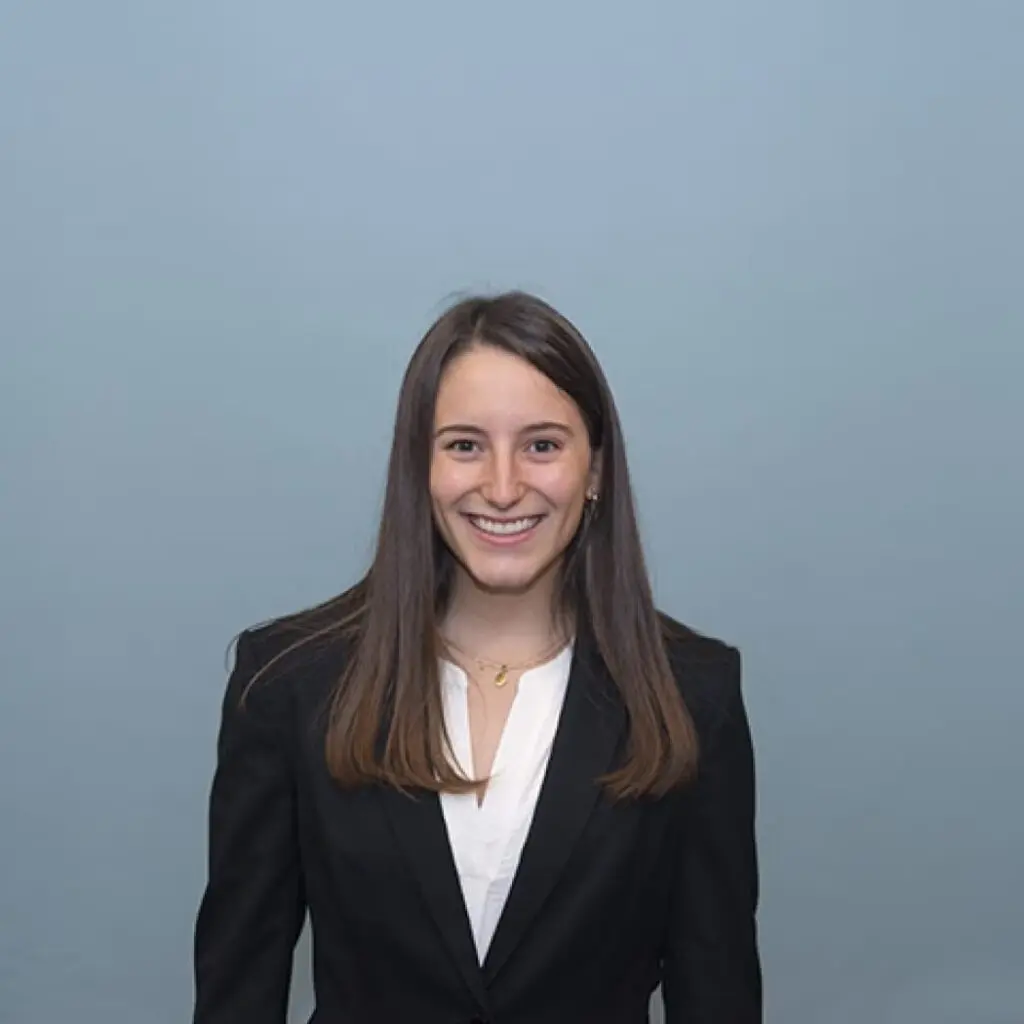 Maya Burns wearing a black blazer and a white button-down shirt with a gold necklace.