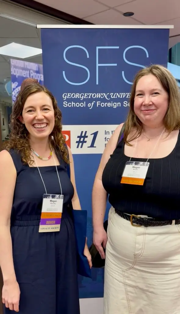 Two individuals standing in front of a Georgetown University School of Foreign Service banner, smiling at the camera, both wearing conference badges.