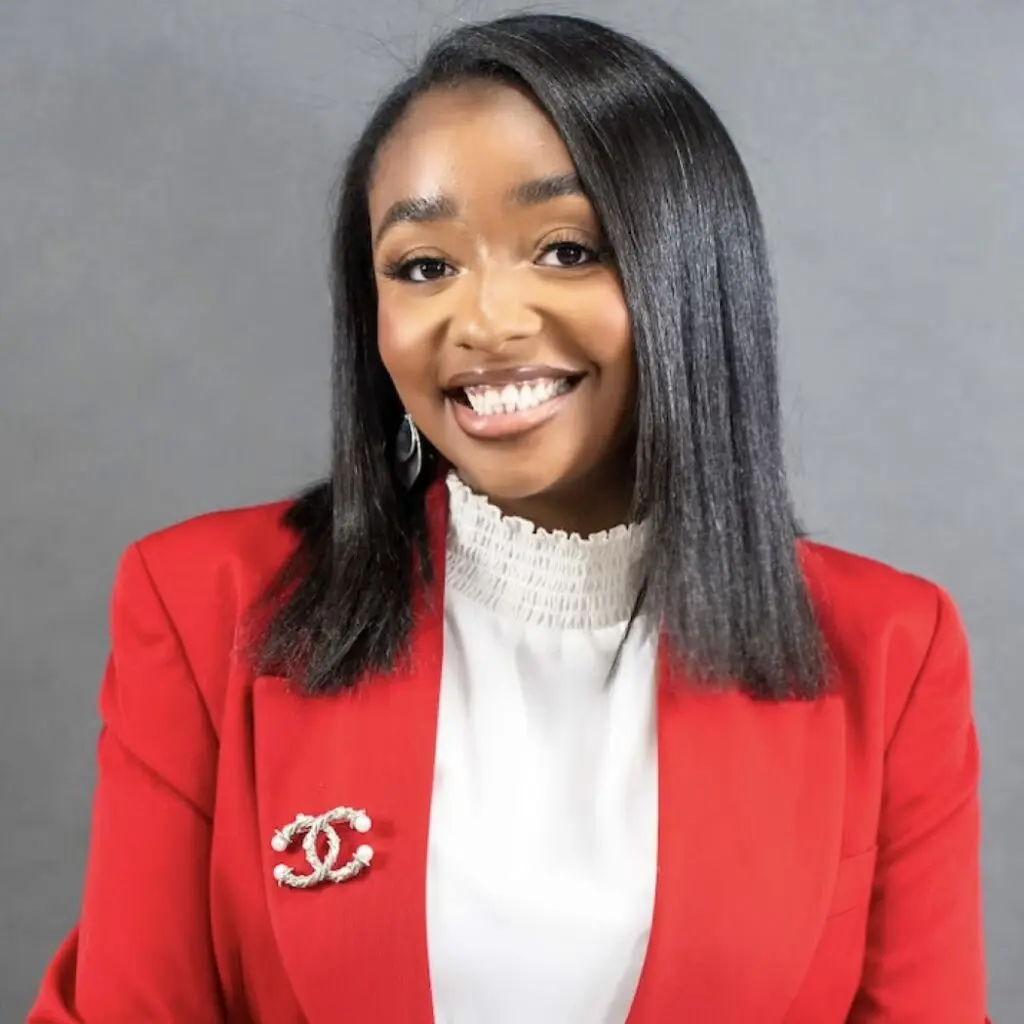 Mia Douglas wearing a red blazer, a white blouse and a Chanel brooch.