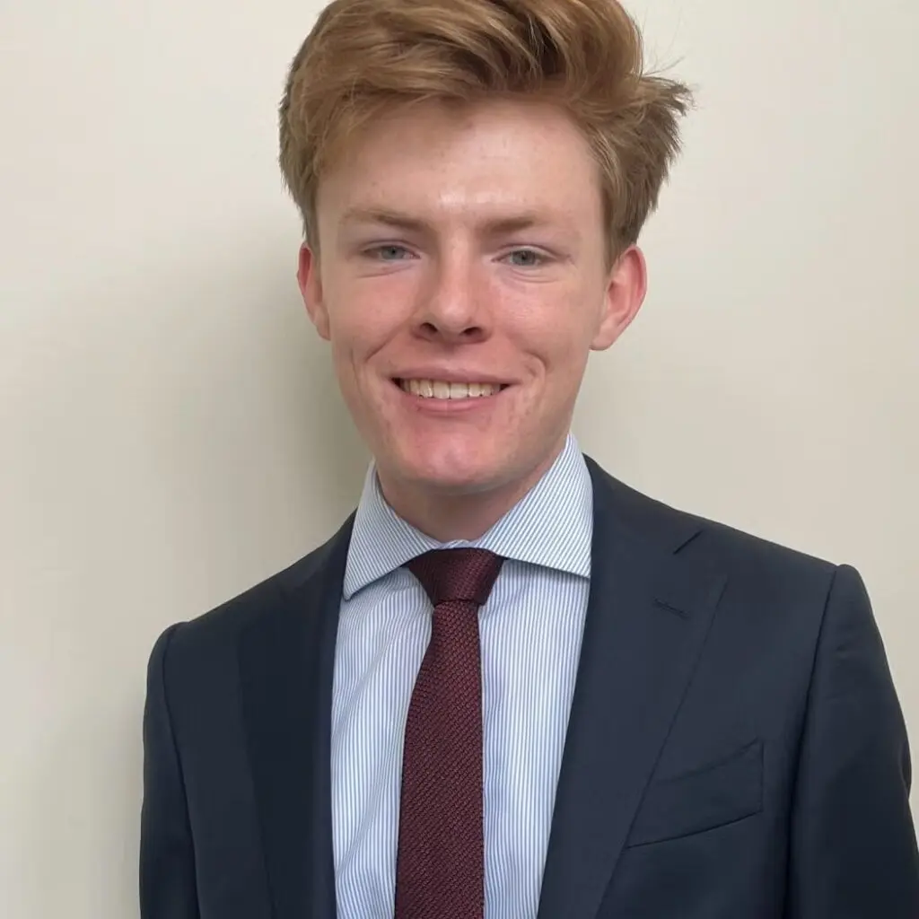 Michael Ball wearing a dark blazer with a button-down shirt and burgundy tie.