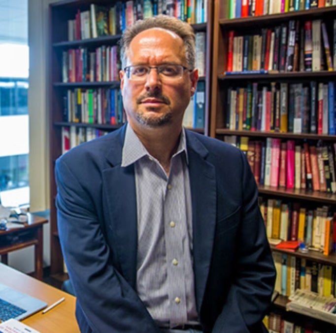 Michael David Fox sitting in his office with bookshelves behind him.