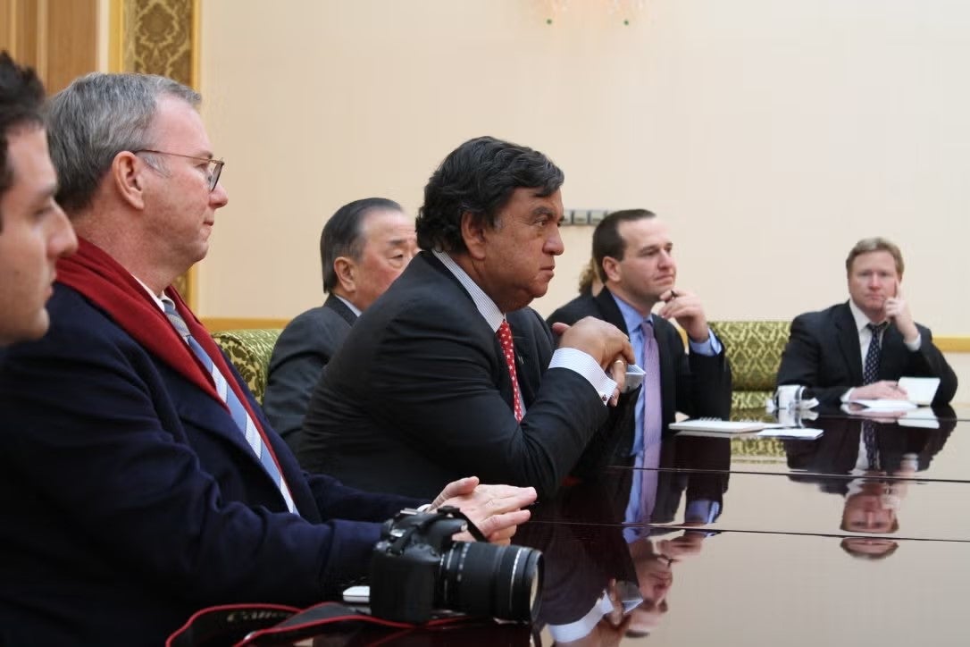 Men sit at long, dark brown table in large room.