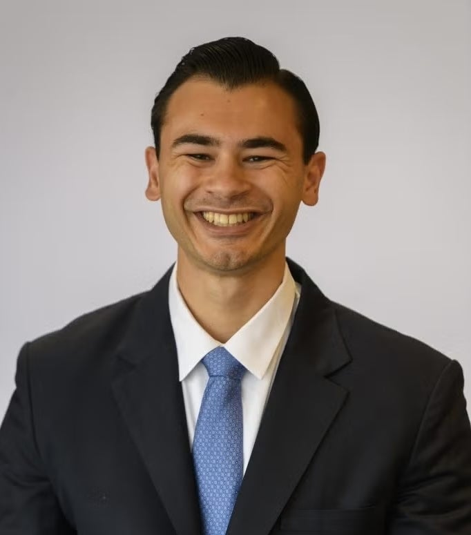 Nathan Kumar wearing a black suit and light blue tie.