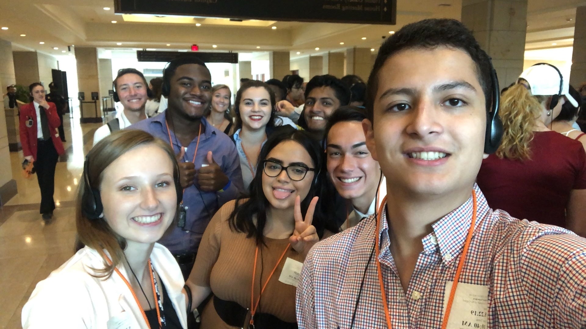 Nicole Sanchez stands with a large group of of students with lanyards and headphones on.