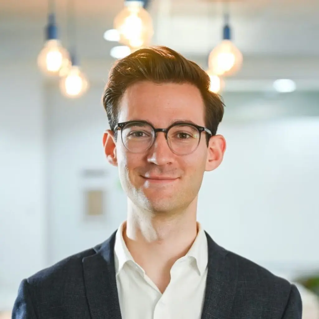 Niel Swanepoel wearing a gray blazer, a white, button-down shirt, and glasses.