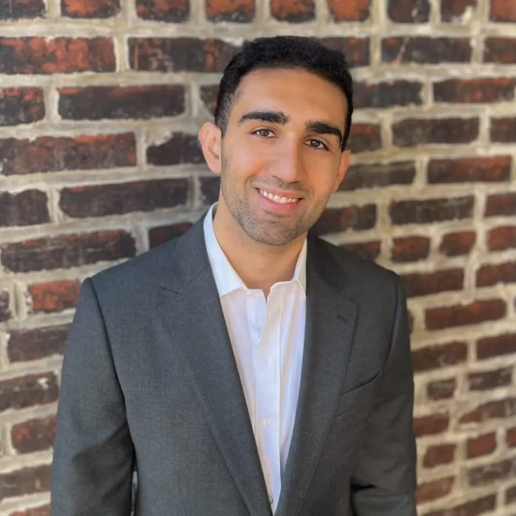Ramin Farrokhi wearing a gray blazer and a white button-down shirt against a brick background.