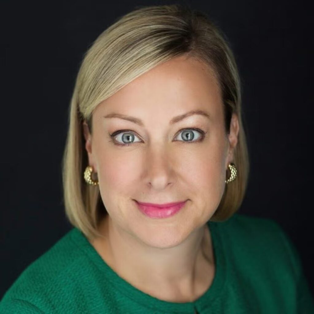 Headshot of Rebecca Patterson wearing a green shirt and gold hoop earrings on a black background.