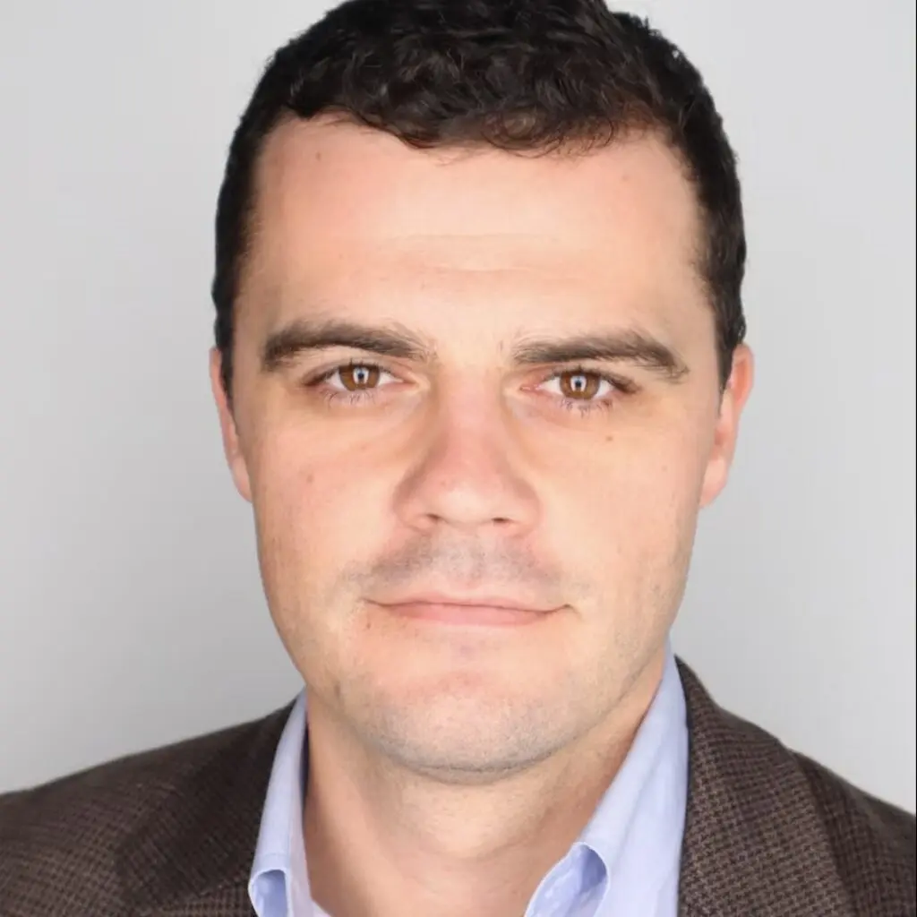 Reed Collins wearing a dark blazer and a light blue button down shirt.