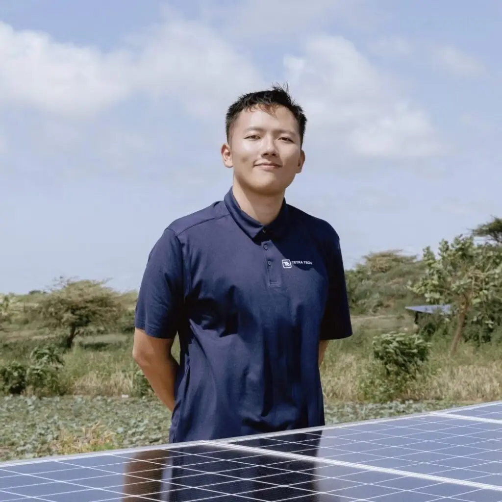 Ruobin Liu standing beside solar panels, wearing a black polo shirt.