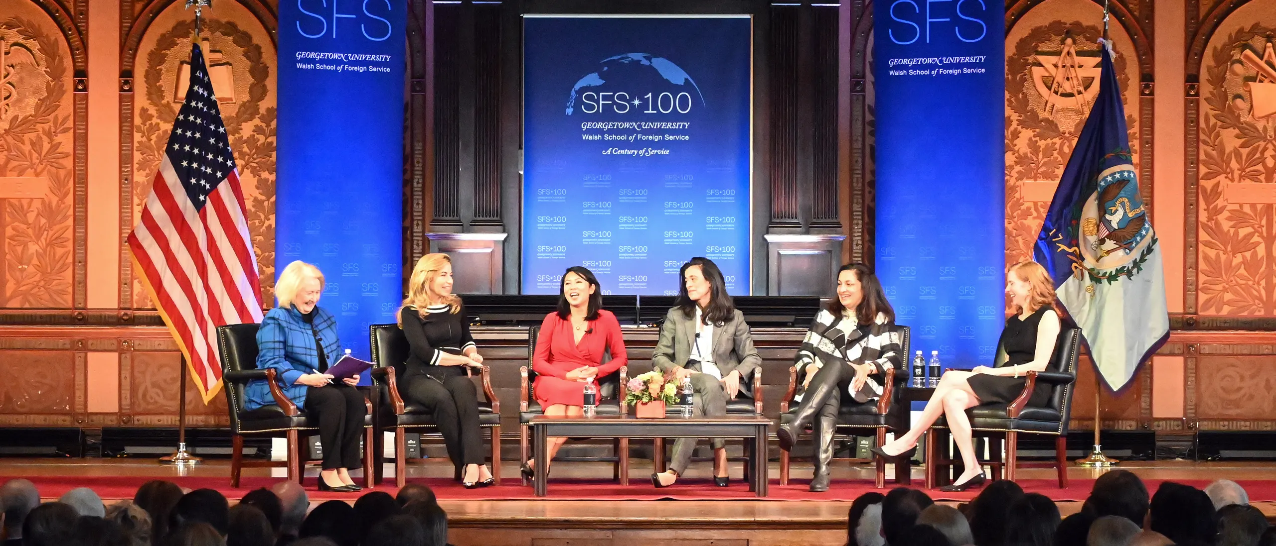 Six women speaking in a panel on stage. Behind them, banners for the SFS 100. In front of them an audience.