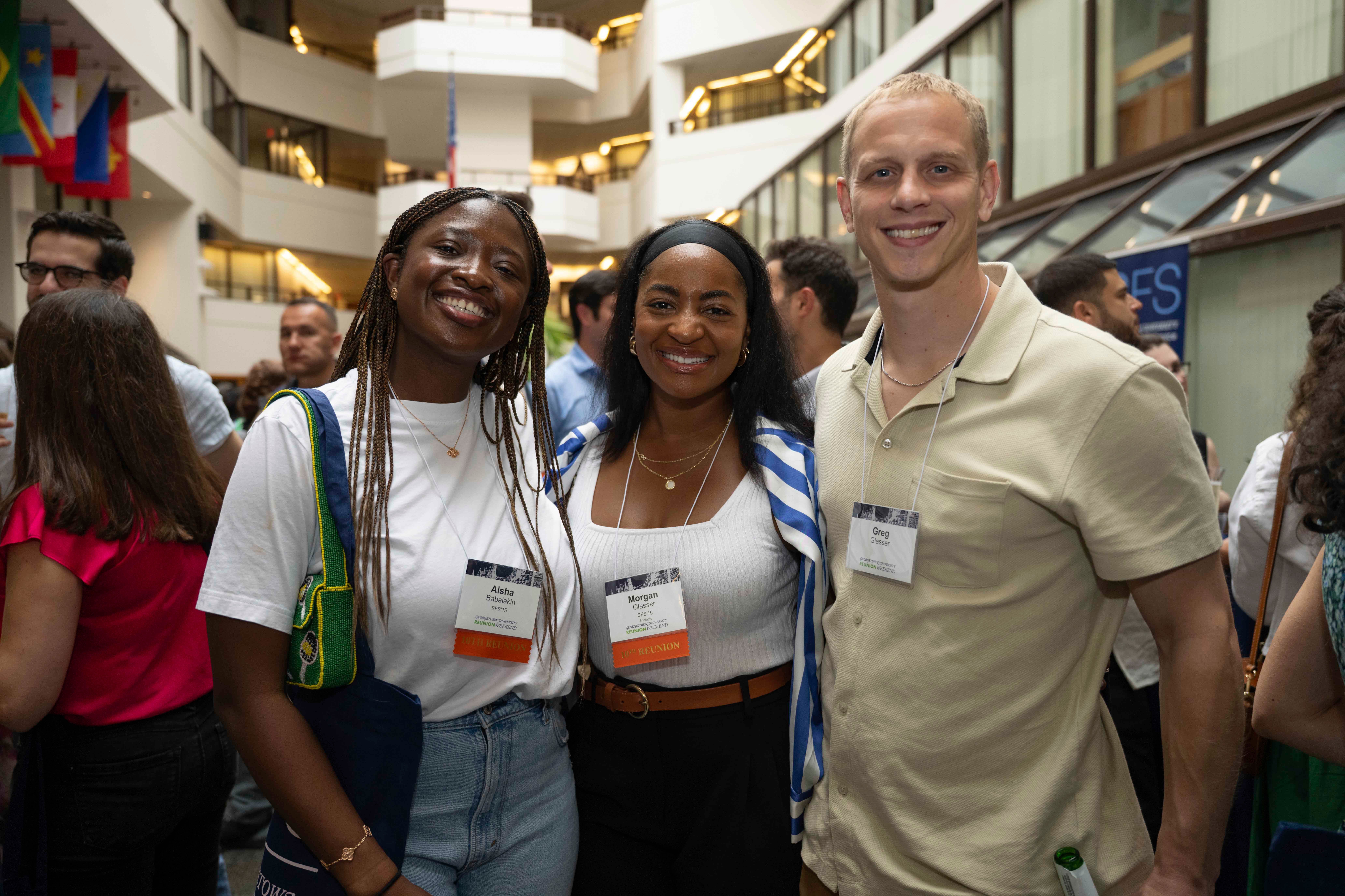 Three individuals smiling at a networking event, each wearing badges with visible names and affiliations.