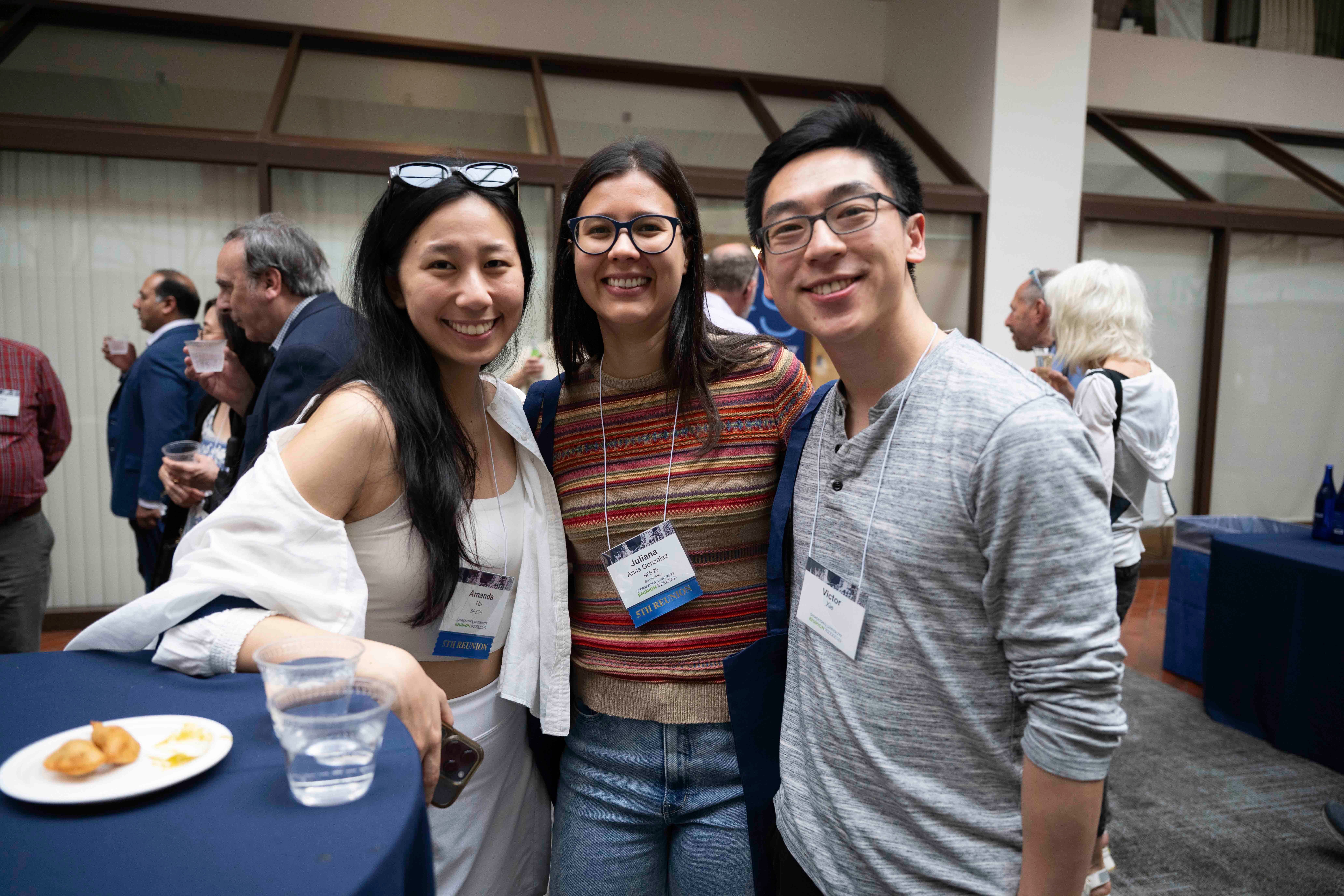 Three people smiling at a networking event, two wearing name tags and one holding a plate of food.
