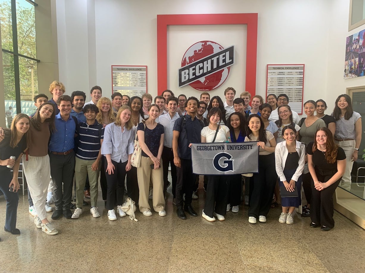 Sam Li stands with his Business and Global Affairs cohort holding a Georgetown University banner in front of a sign that says, "Bechtel."