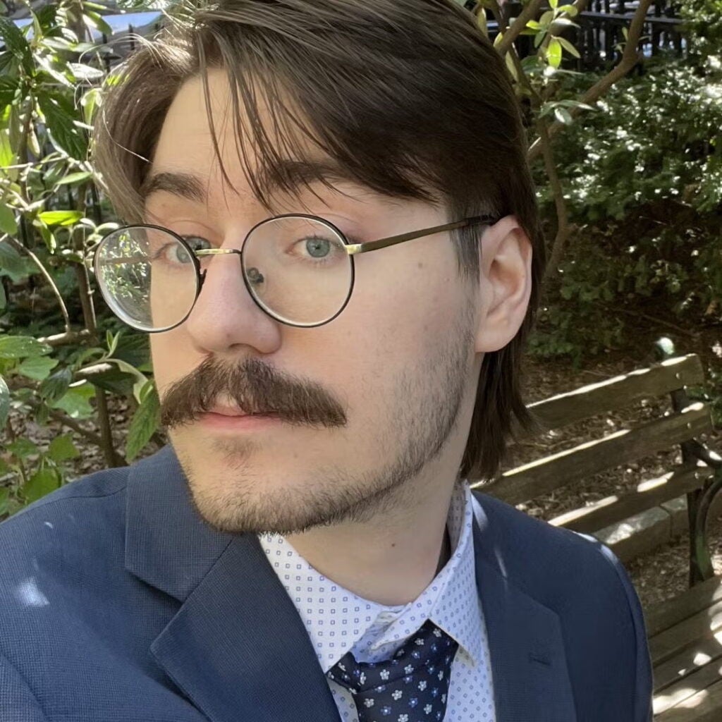 Sebastian Kopec wearing a blue blazer, glasses, and a tie.