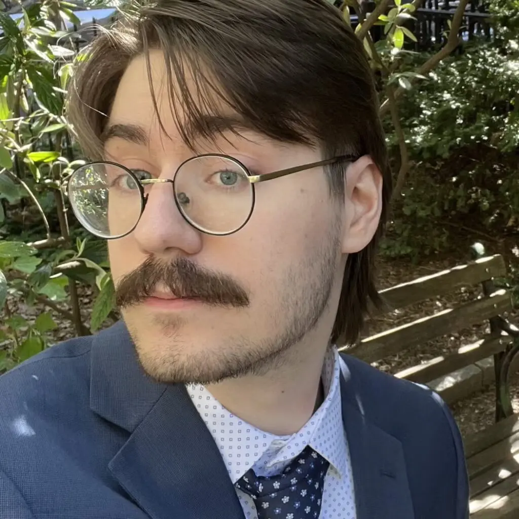 Sebastian Kopec wearing a blue blazer, glasses, and a tie.