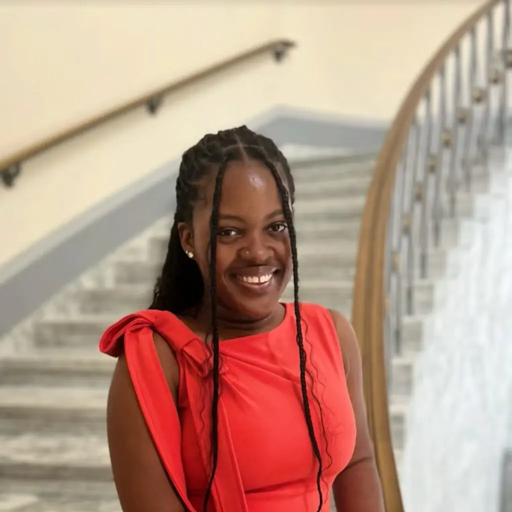 Sheyann Barnett standing on a staircase, wearing a red blouse with a bow on the shoulder.