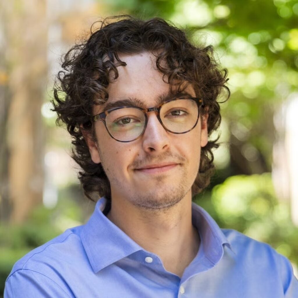 Sidney Dispas wearing a blue button-down shirt and glasses.