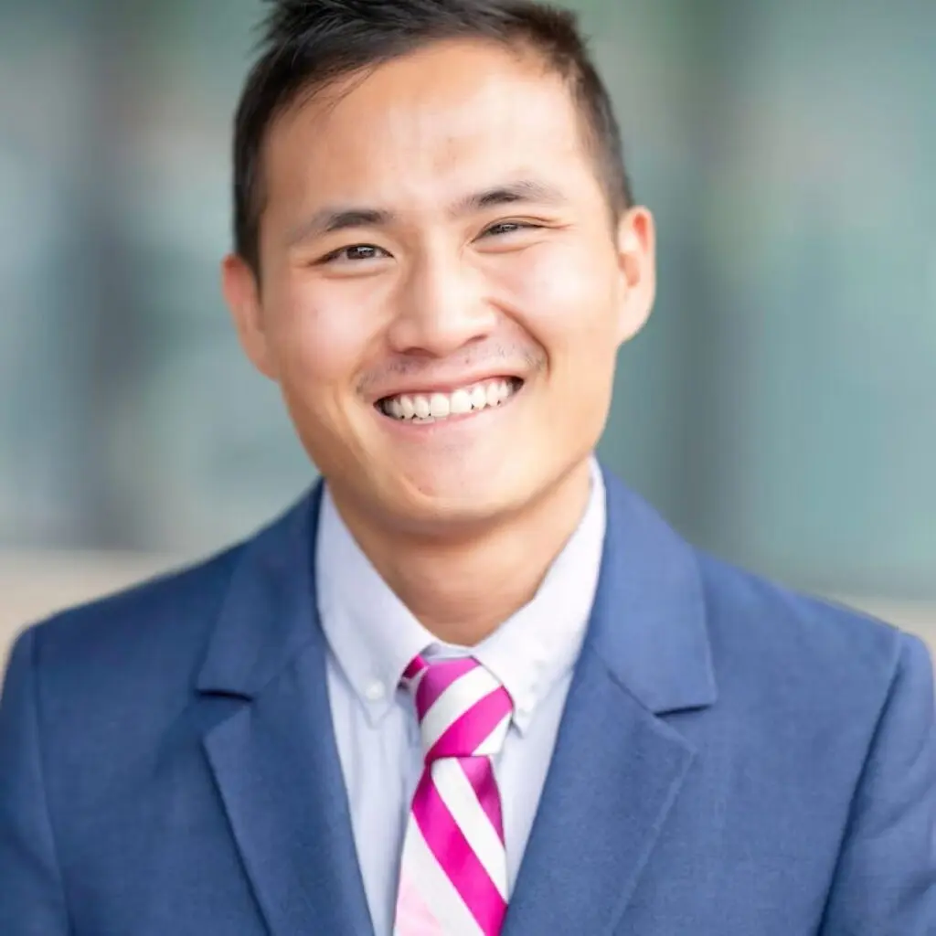 Trey Spadone wearing a blue suit, white button-down shirt and white and magenta striped tie.