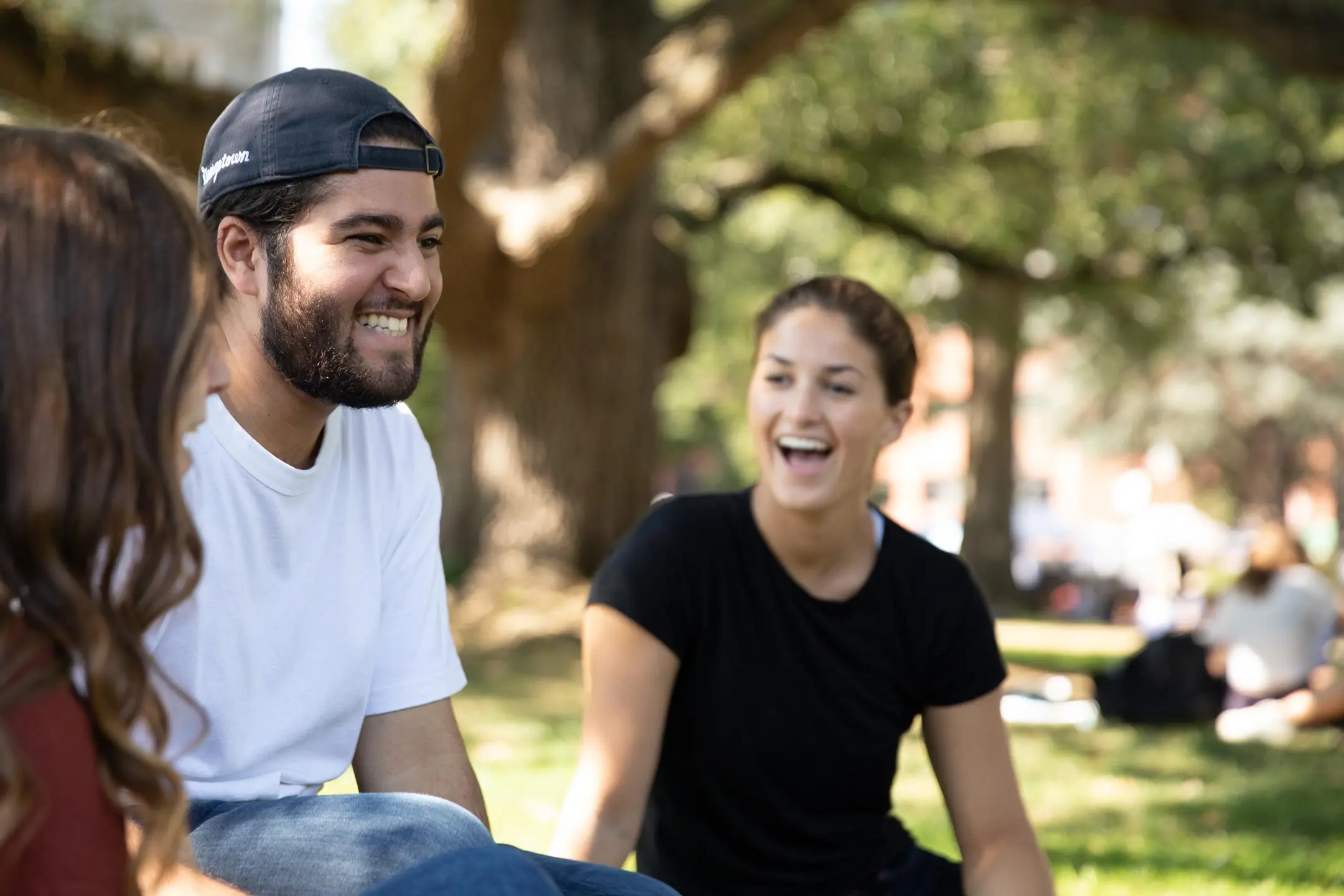 Three students sitting on the lawn smiling at each other