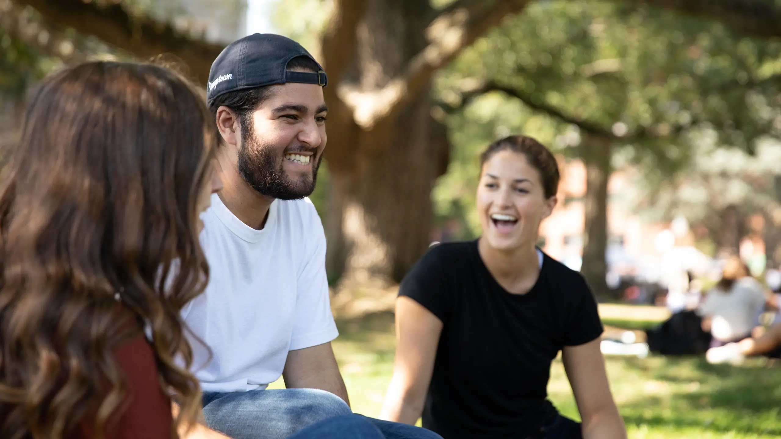 Three students sitting on the lawn smiling at each other