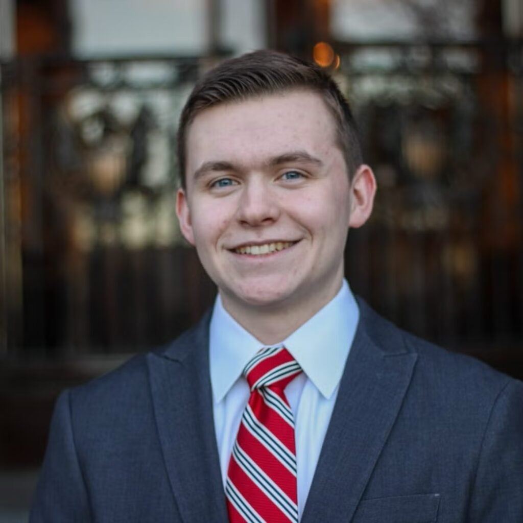 William Doran wearing a navy blue blazer and a red striped tie.