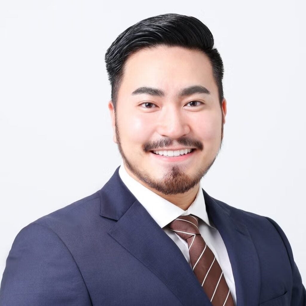 Yoshihiro Komori wearing a navy blue blazer and a brown striped tie.